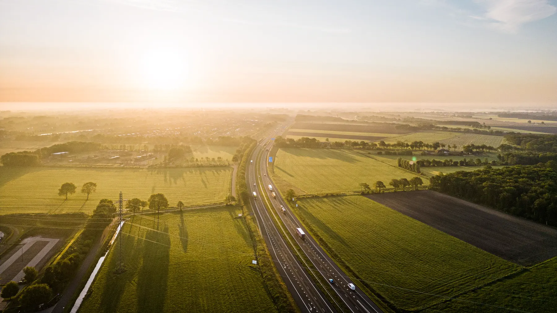 Sunrise over green fields with a motorway running through them